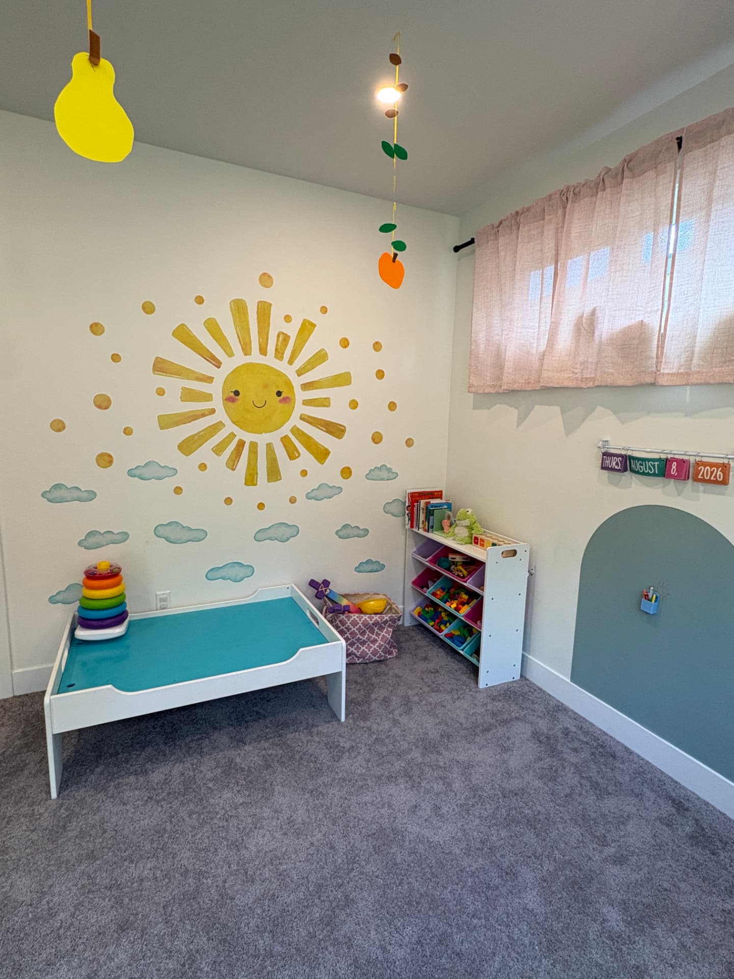 The El Nidito playroom with a cheerful painted sun mural, cozy cot, and shelves of toys